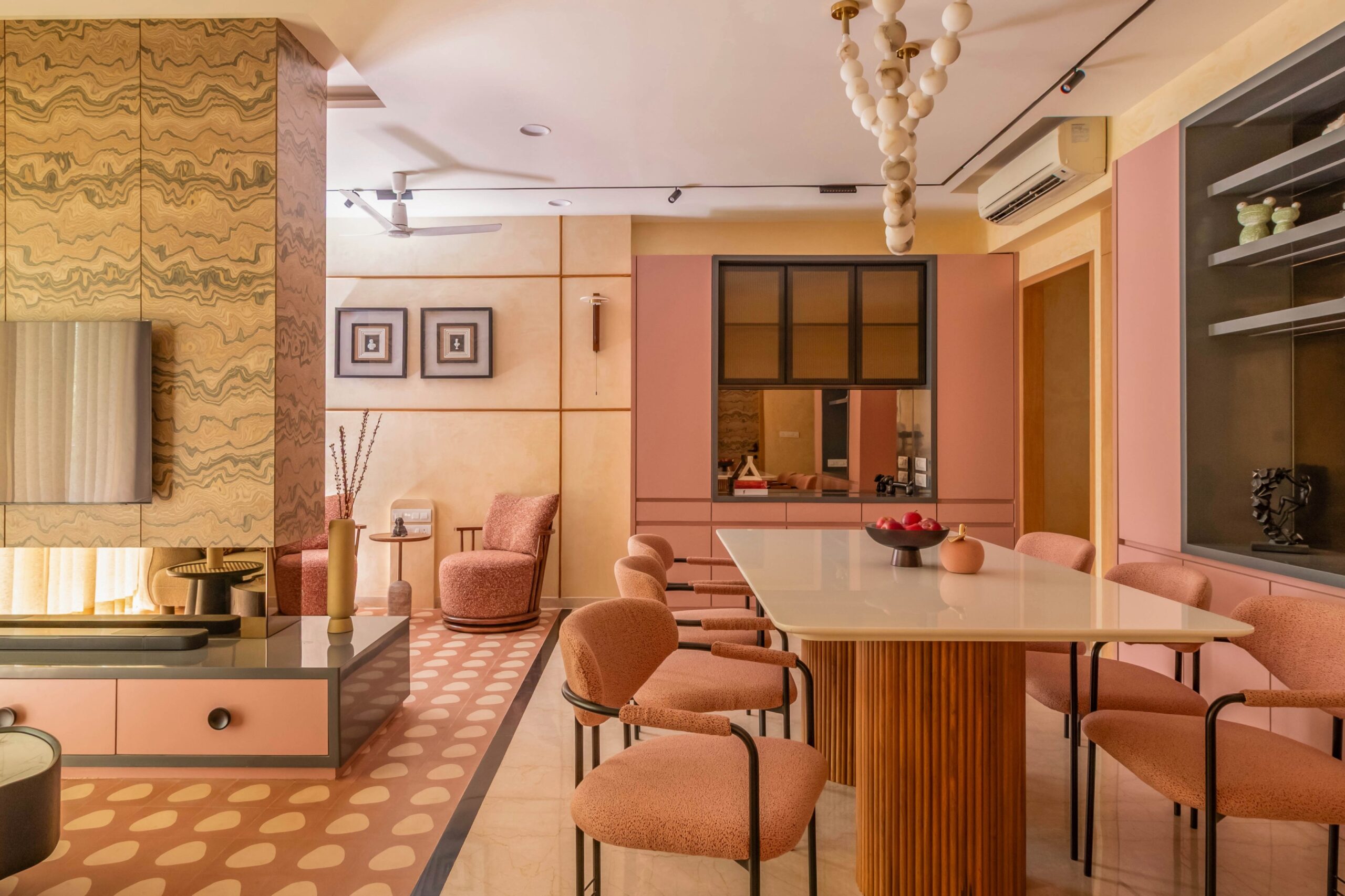 Modern dining room featuring a fluted dining table base, upholstered dining chairs, custom pink cabinetry, designer lighting, and warm contemporary interiors.