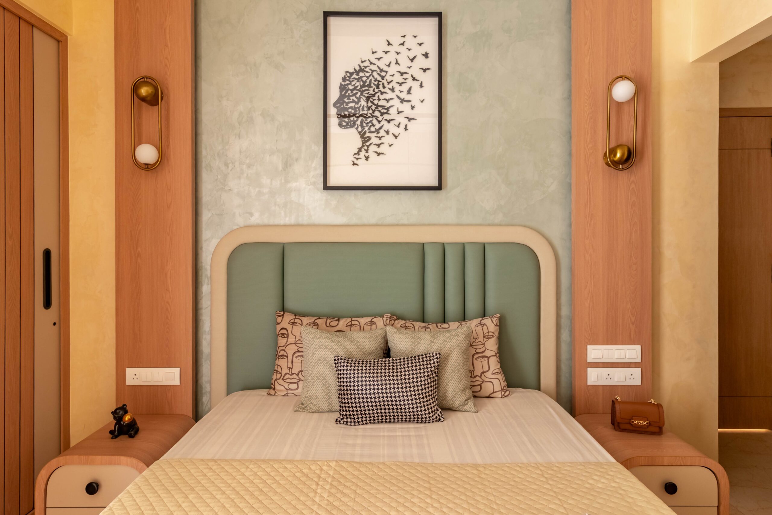 Modern Indian bedroom featuring a mint green upholstered headboard, textured accent wall, wooden side panels, designer wall sconces, and contemporary décor in warm neutral tones.
