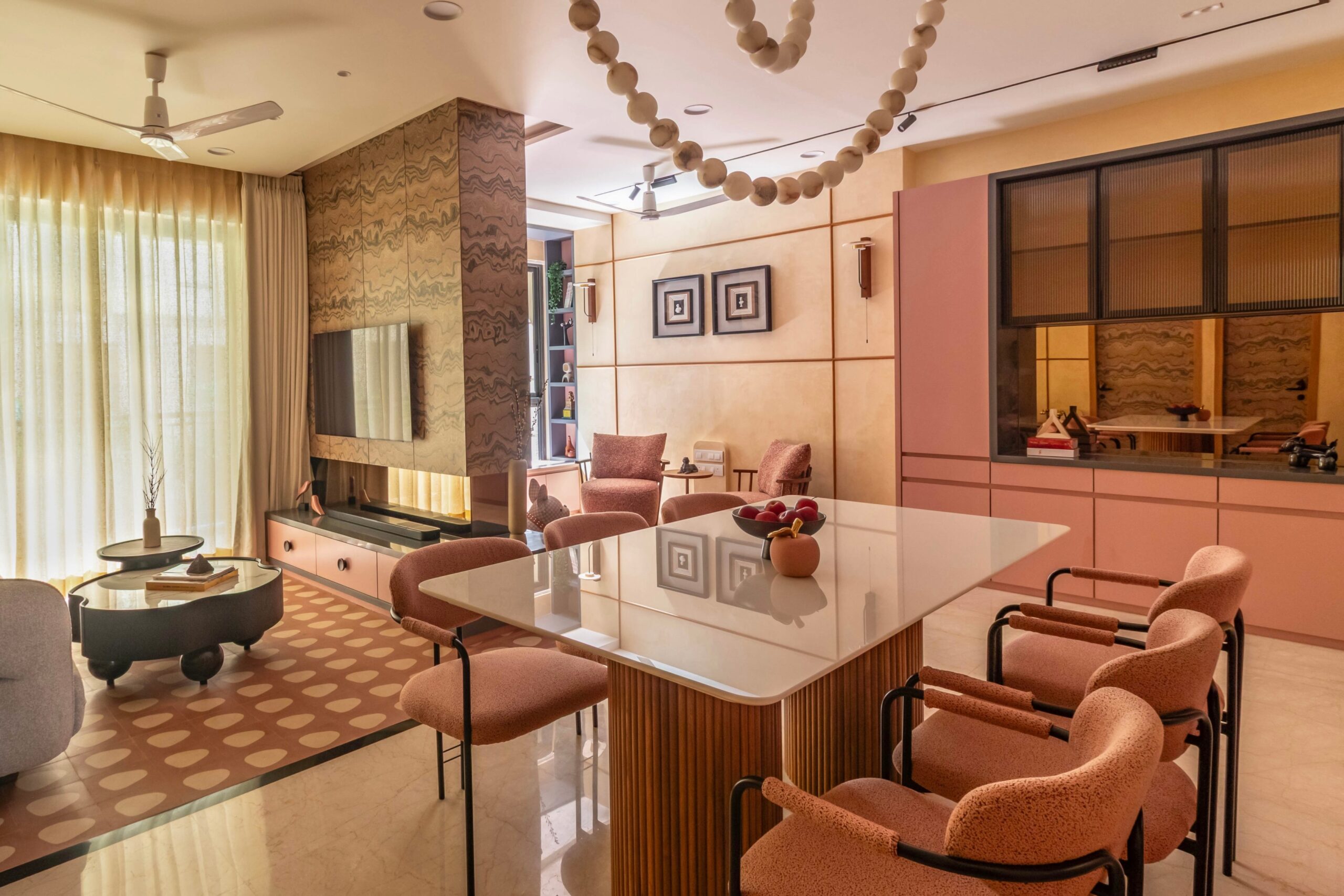 Open-plan living and dining area in a modern Indian home featuring a large dining table, designer TV unit, custom cabinetry, warm textures, and abundant natural light.
